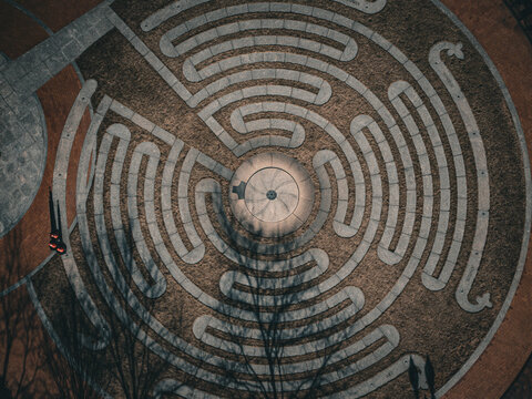 Aerial view of an intricate circular labyrinth pattern etched into the earth, a blend of light stone and dark soil creating a mesmerizing contrast, Boston, Massachusetts, United States.