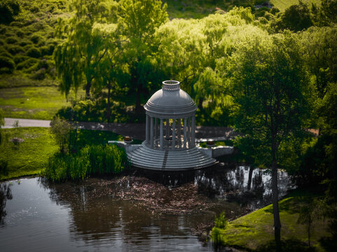 Aerial view of a serene gazebo reflecting in the tranquil pond, enveloped by lush greenery and vibrant trees, a peaceful scene, Boston, Massachusetts, United States.