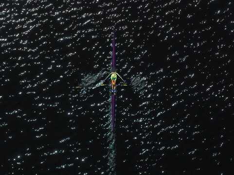 Aerial view of a lone rower slicing through the dark, shimmering waters, leaving a delicate white wake behind them, Boston, Massachusetts, United States.
