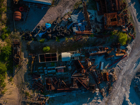 Aerial view of a cluttered junkyard filled with rusty metal debris, old tires, and discarded materials creating a stark contrast against the green patches, Boston, Massachusetts, United States.