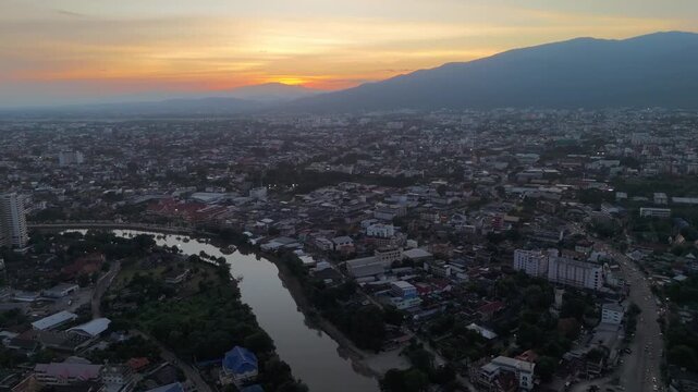 Peaceful golden sunset over Mae Ping River in Chiang Mai. Silhouette of Doi Suthep mountain and calm water reflections in warm evening light