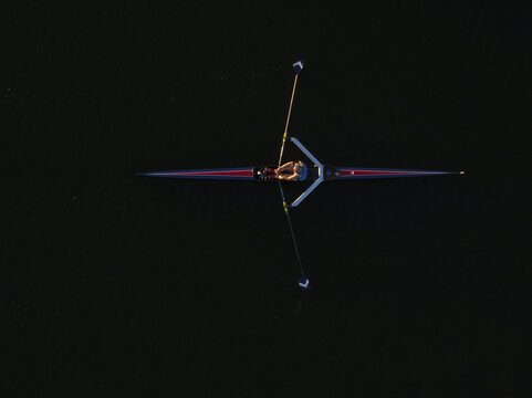 Aerial view of a lone rower gliding across the dark, reflective waters, oars extended like delicate wings, Boston, Massachusetts, United States.