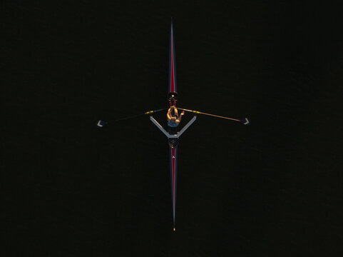 Aerial view of a lone rower slicing through the inky black water, their oars creating a rhythmic dance, Boston, Massachusetts, United States.
