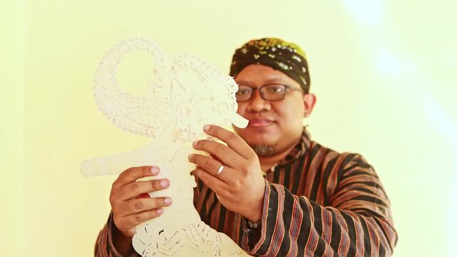 Javanese man in traditional clothing holding a Wayang Kulit puppet