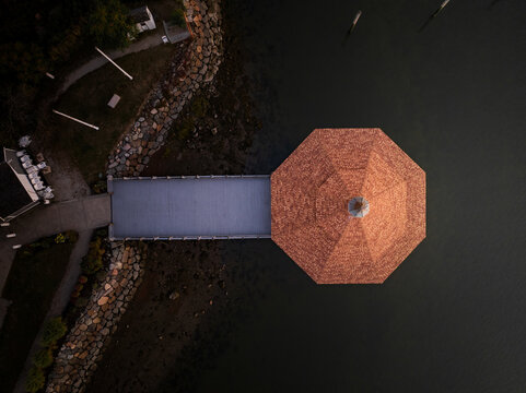 Aerial view of a gazebo with an orange roof over the water, contrasting with the dark tones of the surrounding water and rocky shoreline, Boston, Massachusetts, United States.
