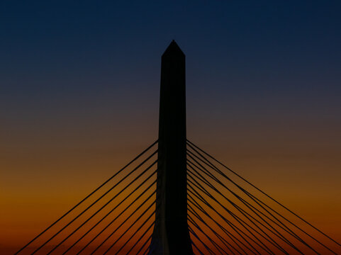 Aerial view of the Zakim Bridge at dusk, its cables stretching like harp strings against the fading light, a silhouette against the fiery sky, Boston, Massachusetts, United States.