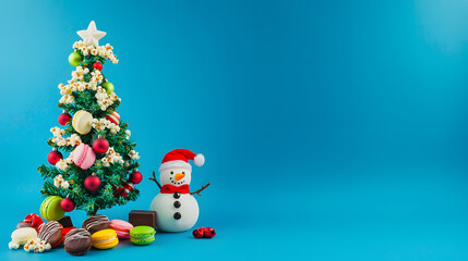 A snowman stands next to a Christmas tree decorated with popcorn, cookies, macarons, and sweets, against a blue studio background with ample copy space