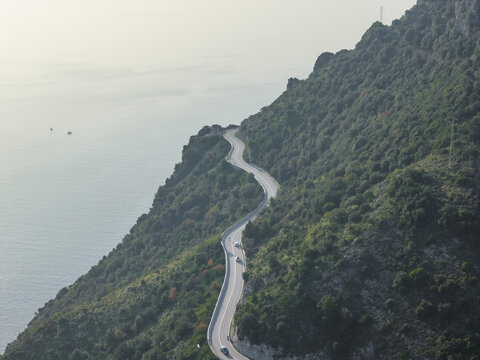 Aerial view of the winding coastal road snaking along the verdant hillside, contrasting with the serene blue sea, Erchie, Amalfi Coast, Italy.