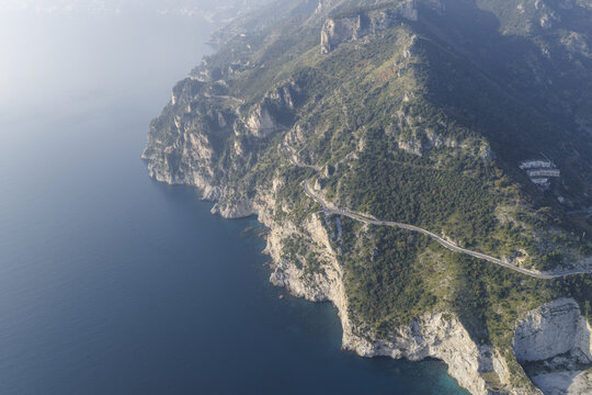 Aerial view of the Amalfi Coast's rugged cliffs meeting the tranquil, deep blue sea, a winding road tracing the verdant coastline, Erchie, Amalfi Coast, Campania, Italy.