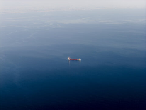 Aerial view of a lone cargo ship cuts through the deep blue expanse of the Tyrrhenian Sea, a stark contrast against the misty horizon, Erchie, Amalfi Coast, Campania, Italy.