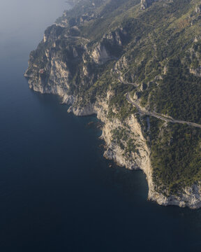 Aerial view of steep cliffs meeting the turquoise sea, a winding road hugging the coastline, nature's raw beauty unfolds, Erchie, Amalfi Coast, Campania, Italy.