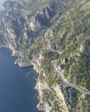 Aerial view of winding coastal roads carve through rugged cliffs, where turquoise waters meet the verdant hillsides, Erchie, Amalfi Coast, Campania, Italy.