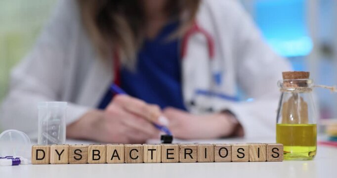 Wooden blocks spell word Dysbacteriosis beside jar with capsules and yellow liquid. Woman doctor studies gut flora balance planning patient therapy