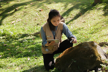 Female botanist examines plant leaves and grass in outdoor field for agricultural eco
