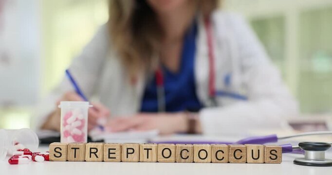 Wooden blocks spell word Streptococcus near capsule containers and chart on table. Woman doctor writes report studying bacterial throat infection