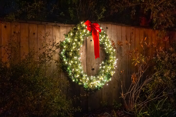 A Christmas wreath, decorated with lights and a red bow, hangs on the fence.
