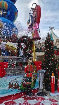 Paris, France - December 10, 2025 Festive outdoor amusement park at the Tuileries Christmas Market, with a Nutcracker soldier stands under simulated snow beside a Christmas tree and a holiday carousel
