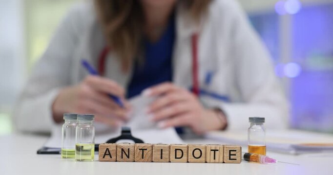Wooden blocks spell word Antidote near glass vials with liquids. Woman toxicology doctor prepares lifesaving dose writing patient emergency protocol
