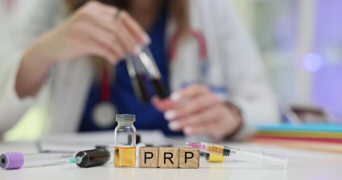 Wooden blocks spell abbreviation PRP beside tubes with dark blood samples. Woman doctor prepares platelet rich plasma recording injection details