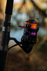 Close-up of a fishing reel with orange line outdoors near water. Shallow depth of field, calm nature scene, fishing and outdoor hobby concept