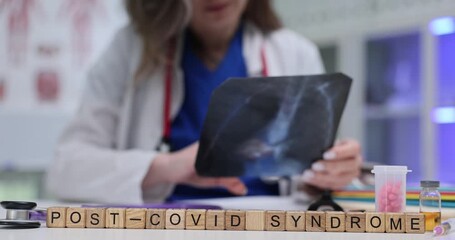 Wooden blocks spell words Post Covid Syndrome on desk. Woman doctor studies chest x-ray picture tracking long term respiratory symptoms in clinic