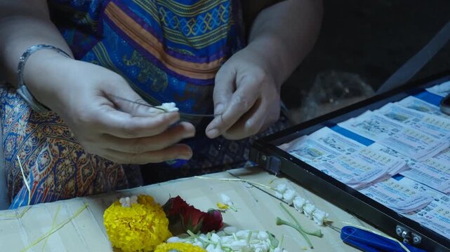 Detailed view of hands skillfully assembling jasmine and marigold flowers into traditional garlands.