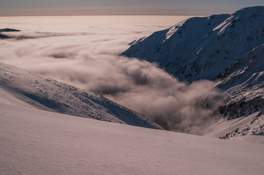 Aerial view of snow-covered peaks piercing through a thick blanket of clouds, the crisp air biting as the sun casts a golden hue, Low Tatras, Banskobystricky kraj, Slovakia.