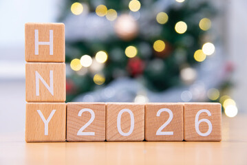 Craft wooden cube blocks HNY 2026 with Christmas tree defocused background. Texts and numbers on wooden blocks with copy space. 2026 happy new year idea concept.