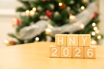 Craft wooden cube blocks HNY 2026 with Christmas tree defocused background. Texts and numbers on wooden blocks with copy space. 2026 happy new year idea concept.