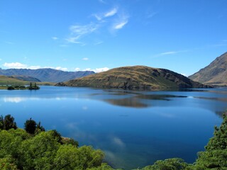 Obraz premium Serene Lake Wanaka landscape with clear reflections, alpine mountains, and blue sky, ideal for travel, nature, and outdoor concepts.
