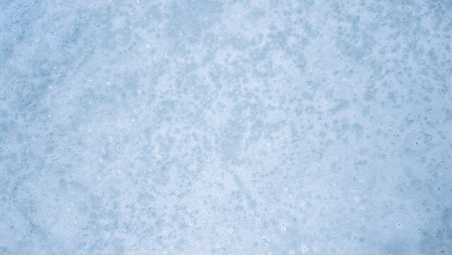 Aerial view of a vast, frozen expanse under the pale sky, the icy surface textured with subtle patterns, creating a tranquil scene, Hofn, Sveitarfelagid Hornafjordur, Iceland.