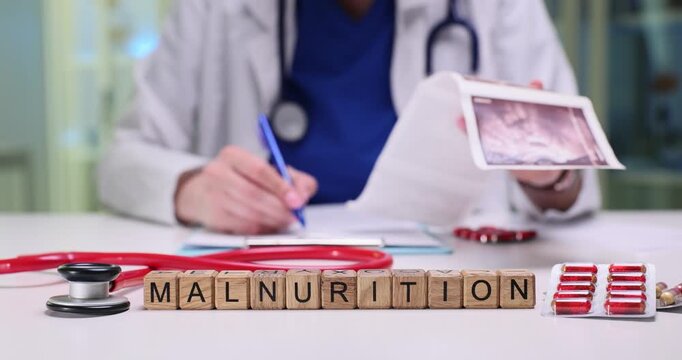 Wooden blocks spell word Malnurition on table in medical office. Doctor in coat studies scan image while writing notes near stethoscope at appointment