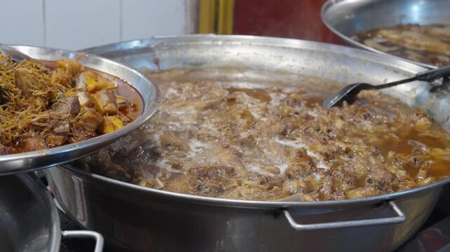 Traditional Asian delicacy, chicken feet cooked in brown sauce, boiling in a large metal pot. Thai street food atmosphere.