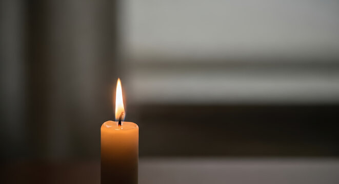 Single burning candle glowing in a dark room. Memorial, hope, and spirituality concept. Atmospheric background with copy space