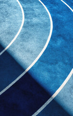 Fototapeta premium Curved white lane lines on a blue athletics track create an abstract composition with dynamic shadows and texture under strong natural lighting.