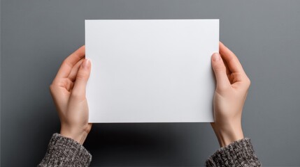 Obraz premium Two hands grasp a blank white sheet of paper with a gray background. This scene takes place indoors during the afternoon with soft lighting