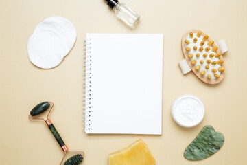 Skincare flat lay with notebook mockup, marble face roller, gua sha, wooden body brush, facial cream and serum
