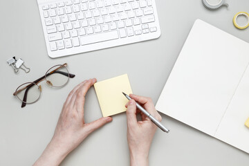 Woman writing on sticky note at organized workspace with notebook and stationery items