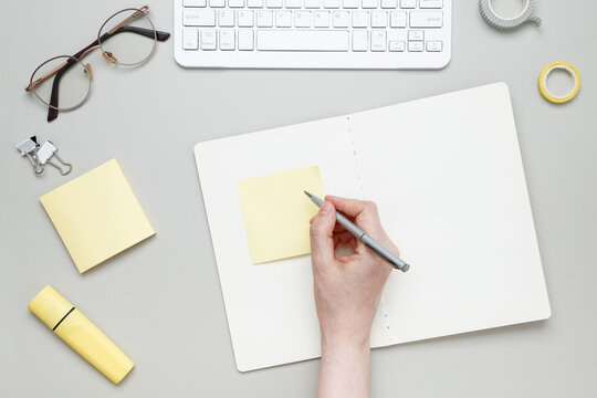 Woman writing on sticky note at organized workspace with notebook and stationery items
