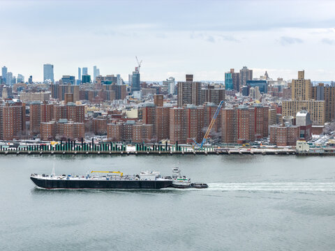 Aerial view of a barge cuts through the steely river, contrasting with the brick buildings and the distant skyline, Brooklyn, New York, United States.