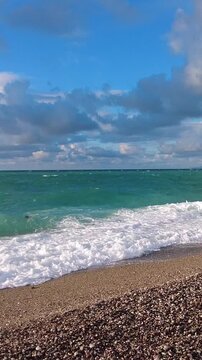 Vertical video of stormy Mediterranean sea: intense waves noisily crash onto the pebble shore of Konyaalti Beach, Antalya. The sky is heavy and cloudy