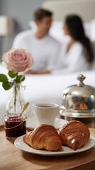 breakfast couple scene with wooden bedside table, two croissants, espresso cups, jam jar, pink rose and cloche in warm morning light