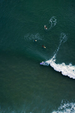 Aerial view of surfers riding the waves, the ocean's dark hues contrasting with the white foam trails, Anglet, Nouvelle-Aquitaine, France.