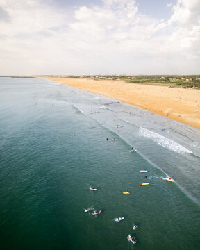 Aerial view of surfers dotting the turquoise waters near the sandy beach, a coastal tapestry of summer activity, Anglet, Nouvelle-Aquitaine, France.