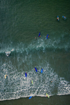 Aerial view of surfers and their boards scattered across the beach break, where foamy waves crash onto the sandy shore, Anglet, Nouvelle-Aquitaine, France.