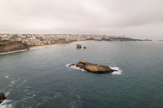 Aerial view of the Rocher de la Vierge standing defiant against the crashing waves of the Atlantic, a contrast to the tranquil beach, Biarritz, Nouvelle-Aquitaine, France.