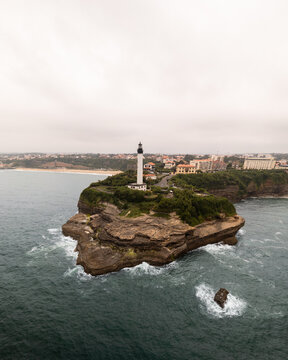 Aerial view of the Virgin Rock topped with a gleaming white lighthouse, surrounded by the turbulent, dark teal waters of the Atlantic, Biarritz, Nouvelle-Aquitaine, France.