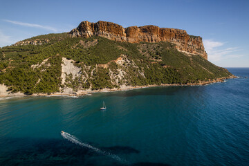 Aerial view of the dramatic Cap Canaille cliffs plunging into the azure sea, a solitary sailboat gliding peacefully below, Cassis, Provence-Alpes-Cote d Azur, France.