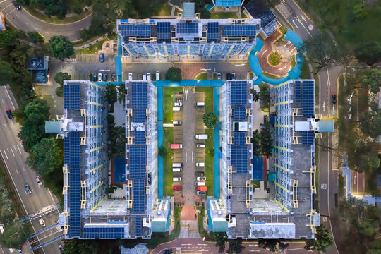 Aerial view of symmetrical Housing Development Board flats adorned with solar panels, casting long shadows and glowing with warm light, Singapore, Singapore.
