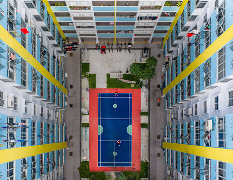 Aerial view of a vibrant courtyard with a striking blue and red badminton court nestled between towering, colorful HDB flats, Singapore, Singapore.
